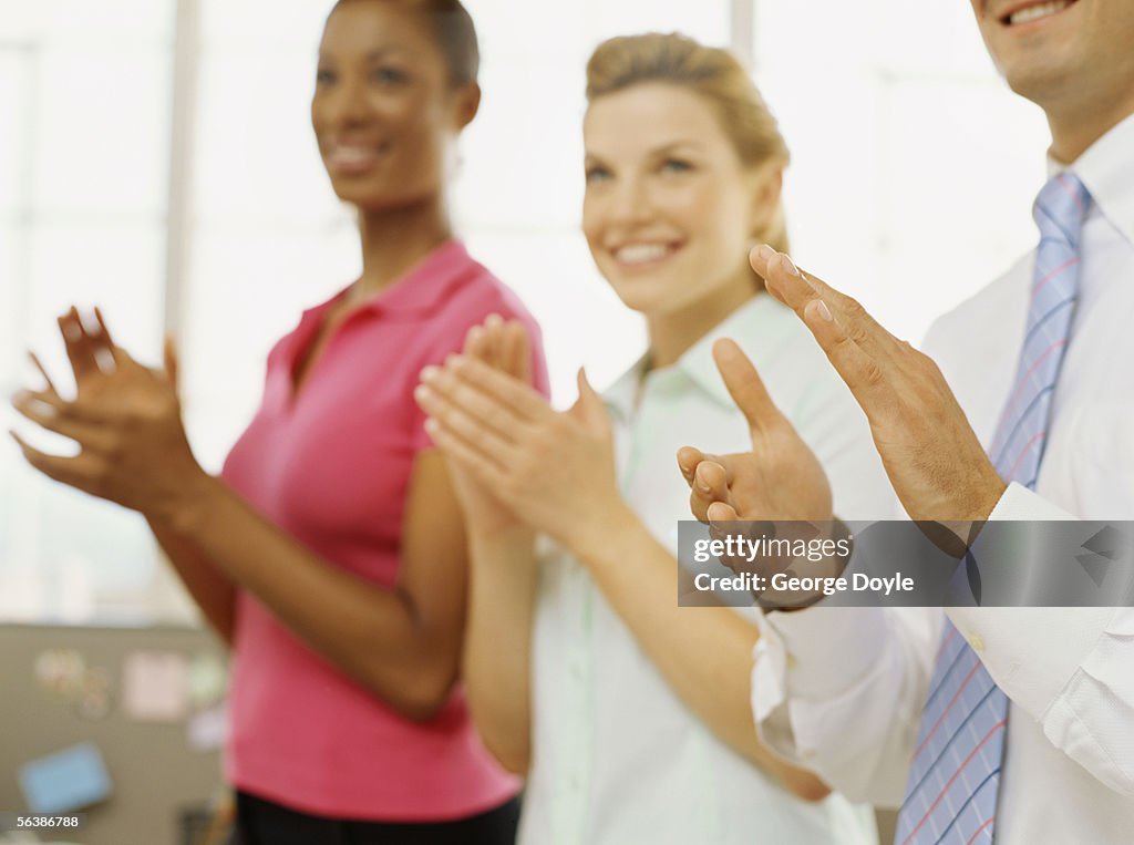 Two businesswomen and a businessman applauding