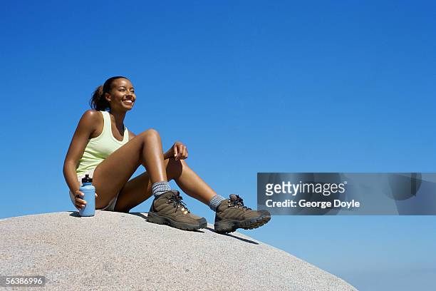 low angle view of a young woman sitting on a rock - botas azules fotografías e imágenes de stock