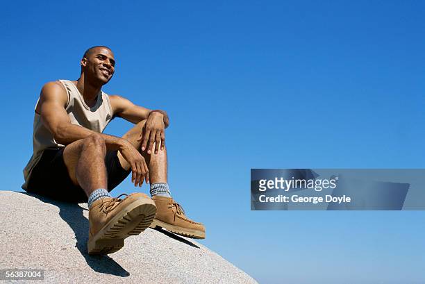 low angle view of a young man sitting on a rock - hand on knee photos et images de collection