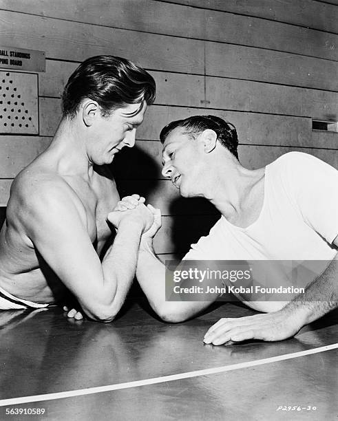 Actors Kirk Douglas and John Payne arm wrestling in a gymnasium, for Paramount Pictures, 1950.