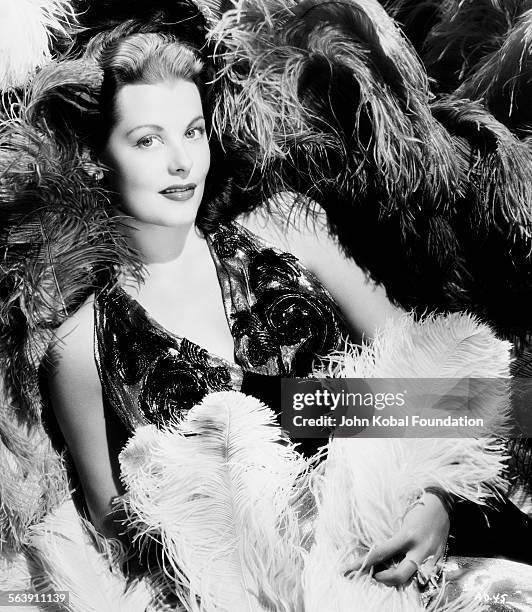 Portrait of actress Arlene Dahl lying amongst a sea of feathers, for Warner Bros Studios, 1946.