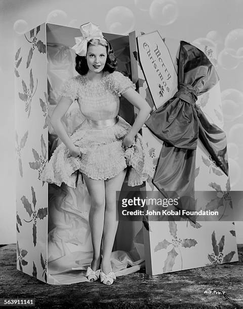 Portrait of actress Arlene Dahl wearing a bow in her hair as she steps out of a huge Christmas present box, for Warner Bros Studios, 1946.