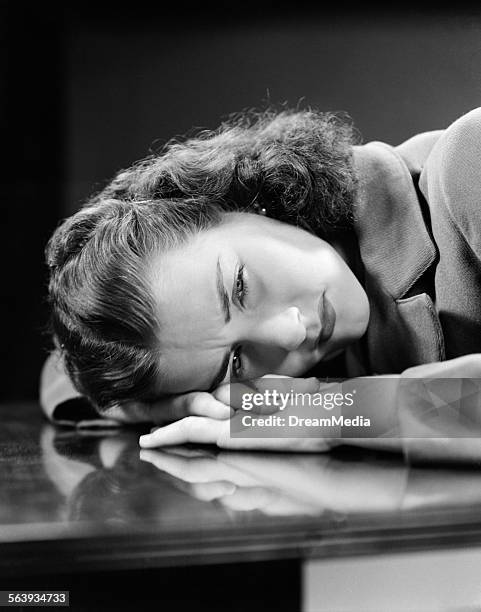 1940s SAD YOUNG WOMAN LYING HEAD ON HER HANDS ON TABLE DESK PAIN SADNESS WORRY