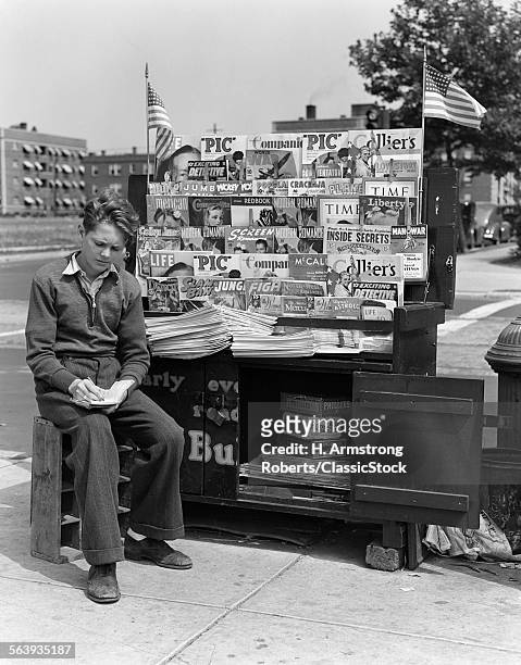 1940s BOY SITTING AT CORNER NEWSSTAND WRITING IN NOTEPAD