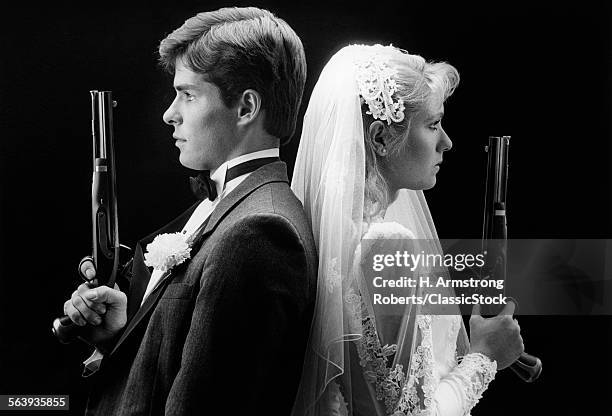 1980s BRIDE AND GROOM STANDING BACK TO BACK HOLDING DUELING PISTOLS