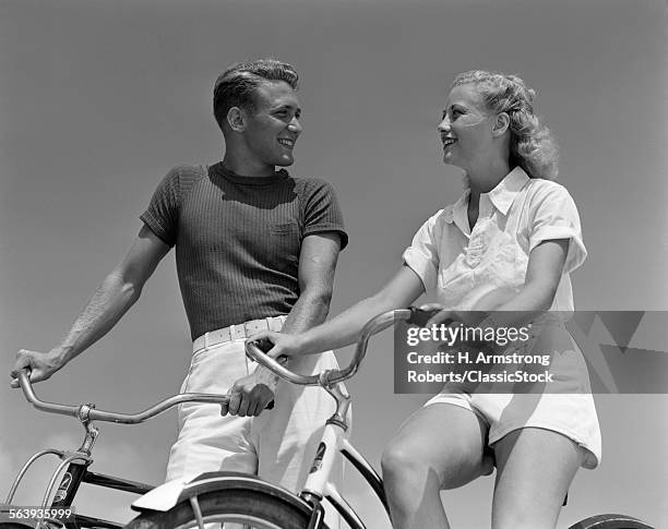 1930s 1940s SMILING BLONDE COUPLE ON BIKES LOOKING AT ONE ANOTHER
