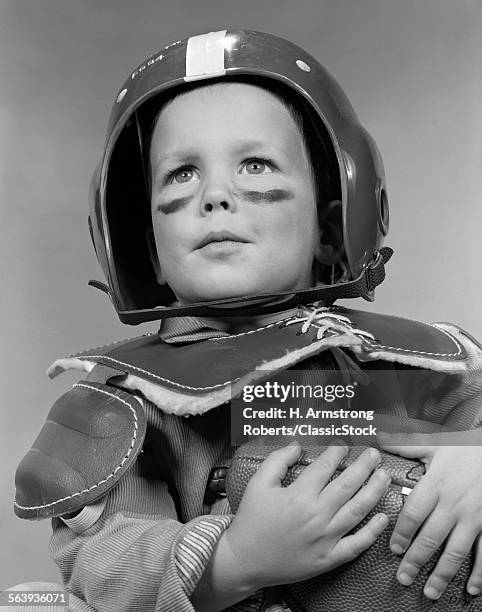 1950s PORTRAIT OF BOY IN HELMET & SHOULDER PADS WEARING GREASE PAINT UNDER EYES & HOLDING FOOTBALL