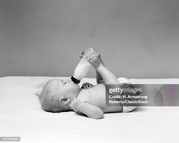 1940s BABY LAYING ON ITS BACK DRINKING FROM MILK BOTTLE HELD WITH FEET