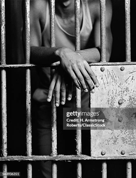 1970s AFRICAN AMERICAN MALE HAND SMOKING CIGARETTE THROUGH THE BARS OF JAIL PRISON CELL