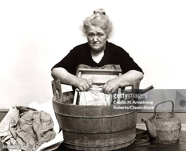 1920s 1930s 1940s SENIOR WOMAN WASHING CLOTHES IN OLD FASHIONED WOODEN TUB AND WASHBOARD