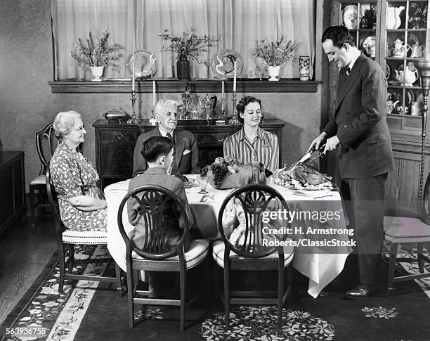 1940s FORMAL DINNER WITH FOUR ADULTS AND TWO CHILDREN ONE MAN STANDING AT HEAD OF TABLE CARVING THE TURKEY