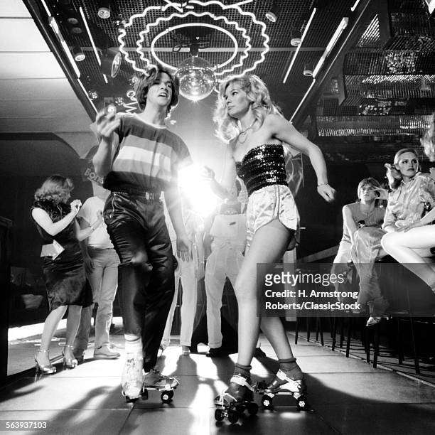 1970s 1980s COUPLE DISCO DANCING ON ROLLER SKATES WEARING TRENDY CLOTHES UNDER A MIRRORED BALL