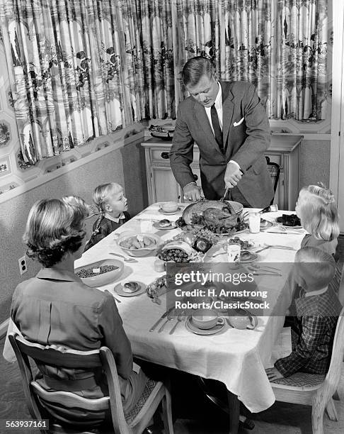 1950s FAMILY OF 5 AT DINING ROOM TABLE FOR THANKSGIVING DINNER WITH FATHER CARVING TURKEY