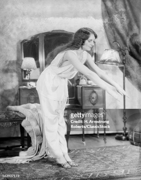 1920s WOMAN EXERCISING BEDROOM WEARING PAJAMAS ARMS STRETCHED OUT BENDING OVER