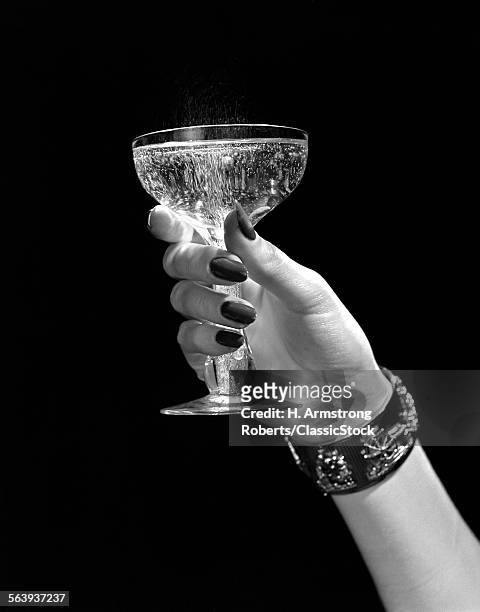 1930s 1940s 1950s WOMAN HAND ORNATE METAL BRACELET HOLDING UP NEW YEAR TOAST GLASS OF CHAMPAGNE AGAINST BLACK BACKGROUND