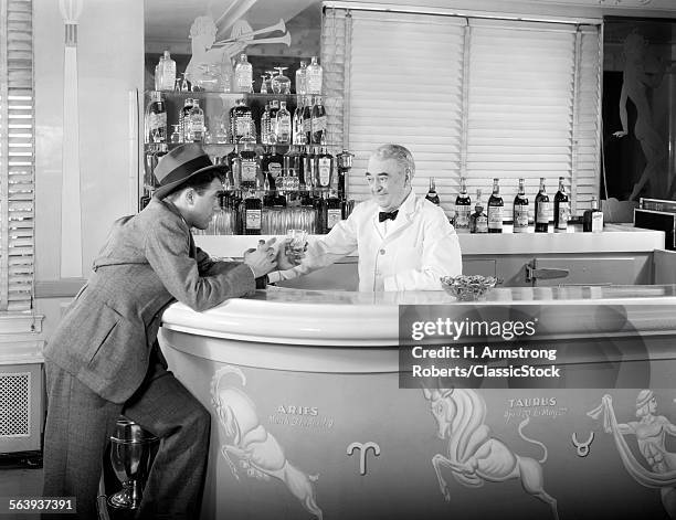 1930s 1940s 1950s MAN LEANING ON BAR ORDERING ANOTHER ALCOHOLIC DRINK FROM BARTENDER IN ART DECO STYLE COCKTAIL LOUNGE