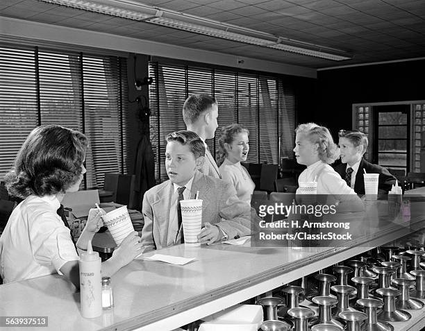 1950s YOUNG TEENAGE GIRLS AND BOYS DRINKING MILKSHAKES SITTING AT SODA FOUNTAIN COUNTER