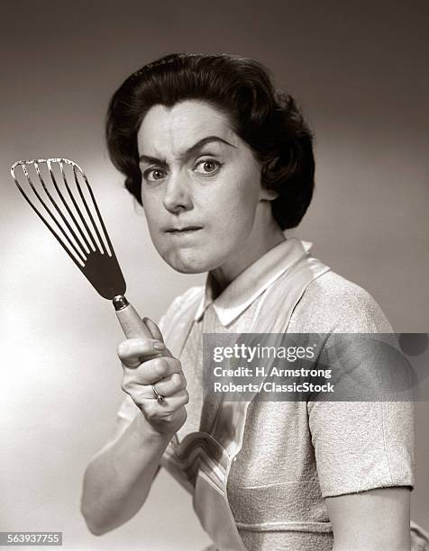 1950s-60s PORTRAIT OF ANGRY HOUSEWIFE BRANDISHING SPATULA AT CAMERA