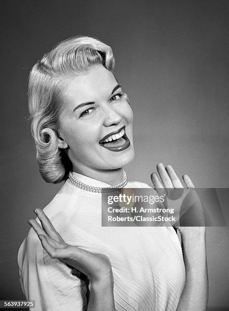 1950s WOMAN WEARING PEARLS SMILING WITH HANDS UP THUMBS TUCKED UNDER ARM