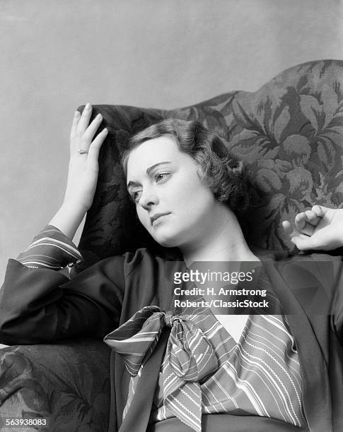 1930s WOMAN SITTING IN HIGH BACK CHAIR WITH A THOUGHTFUL OR MELANCHOLY FACIAL EXPRESSION