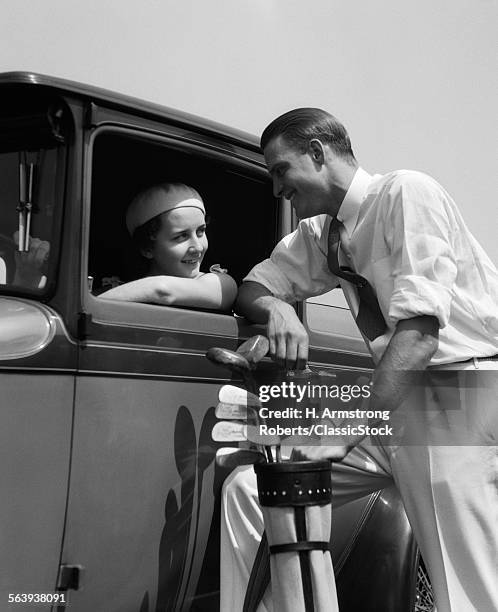 1930s WOMAN IN DRIVER'S SEAT OF CAR LEANING OUT OF WINDOW TALKING TO MAN STANDING HOLDING GOLF BAG