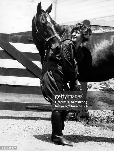 1900s 1910s YOUNG WOMAN WITH UPSWEPT HAIR LIFTING FRONT LEG OF HORSE CHECKING CLEANING HOOF