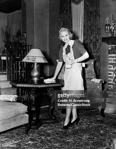 1940s BLONDE WOMAN HOUSEWIFE MAID WEARING APRON CLEANING POLISHING WOODEN END TABLE IN ORNATE LIVING ROOM