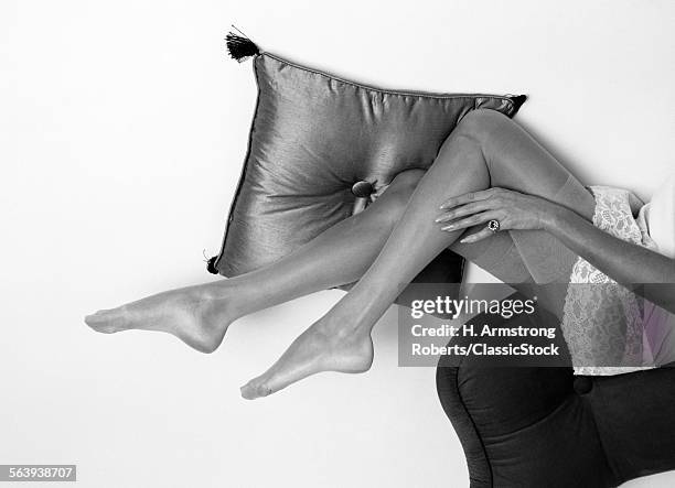 1960s BIRD'S-EYE VIEW OF WOMAN SHOWN WAIST-DOWN IN SLIP & SILK STOCKINGS LYING ON PILLOWS