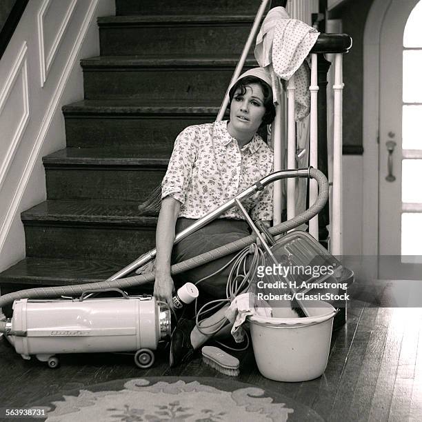 1960s 1970s EXHAUSTED HOUSEWIFE SITTING AT BOTTOM OF STAIRS SURROUNDED BY HOUSE CLEANING EQUIPMENT