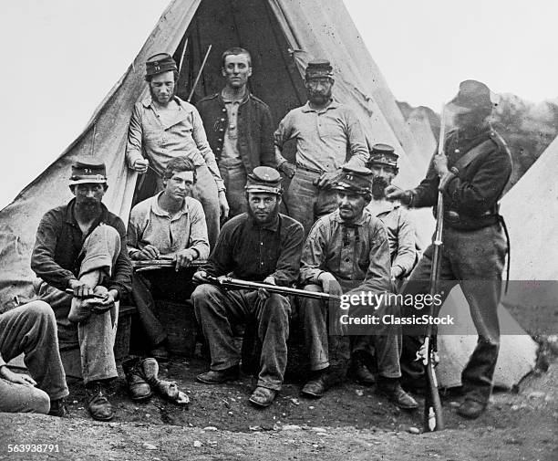 1860s GROUP OF NINE UNION SOLDIERS SEATED IN FRONT OF TENT HOLDING RIFLES LOOKING AT CAMERA