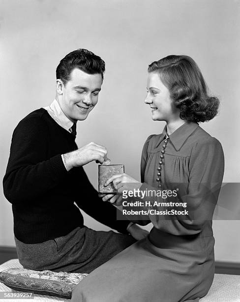 1940s YOUNG TEENAGE COUPLE GIRL HOLDING SMALL BANK BOY DROPPING IN COIN