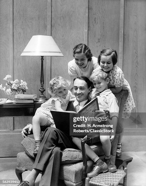 1930s FATHER READING TO FAMILY IN CHAIR