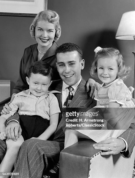 1940s 1950s FAMILY OF FOUR PORTRAIT SITTING IN LIVING ROOM CHAIR LOOKING AT CAMERA