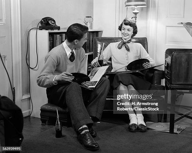 1950s TEEN BOY & GIRL SITTING IN LIVING ROOM DRINKING SODA & LISTENING TO RECORDS