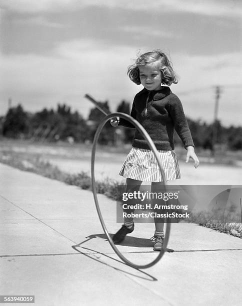 1930s GIRL PLAYING WITH HOOP AND STICK ON SIDEWALK