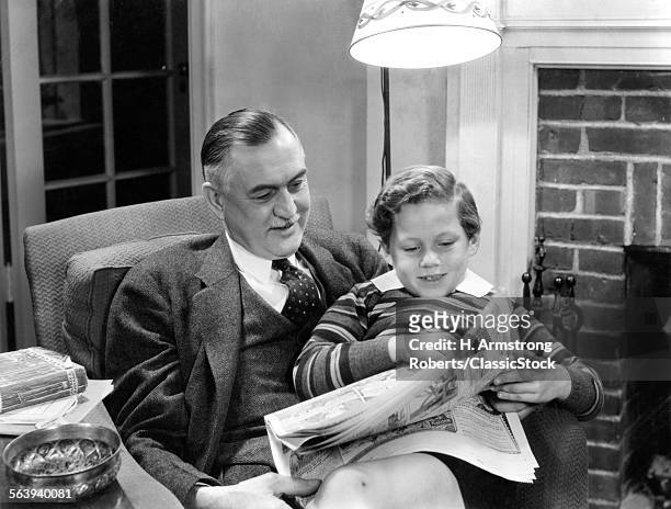 1930s 1940s GRANDFATHER SITTING WITH GRANDSON ON LAP READING SUNDAY NEWSPAPER COMICS TOGETHER IN LIVING ROOM
