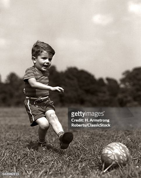 1940s BOY KICKING BALL IN GRASSY FIELD