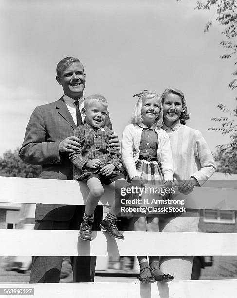 1950s FAMILY PORTRAIT FATHER MAN WOMAN MOTHER GIRL DAUGHTER BOY SON BEHIND BACKYARD FENCE SMILING TOWARDS CAMERA