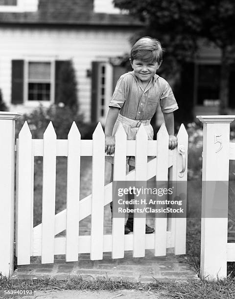 1940s CHILD BOY STANDING SWINGING ON WHITE PICKET FENCE GATE SMILING LOOKING AT CAMERA