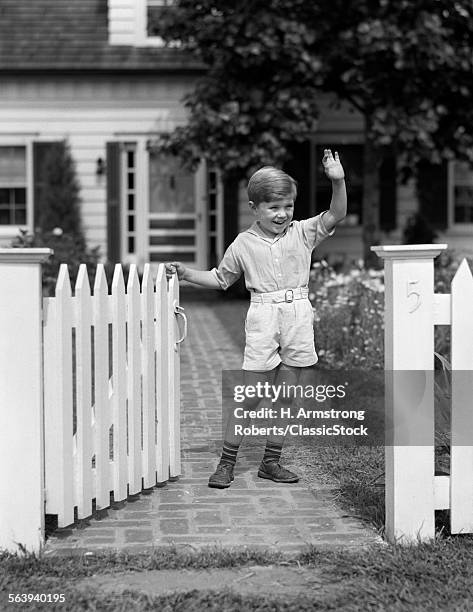 1940s BOY STANDING NEAR WHITE PICKET FENCE GATE WAVING