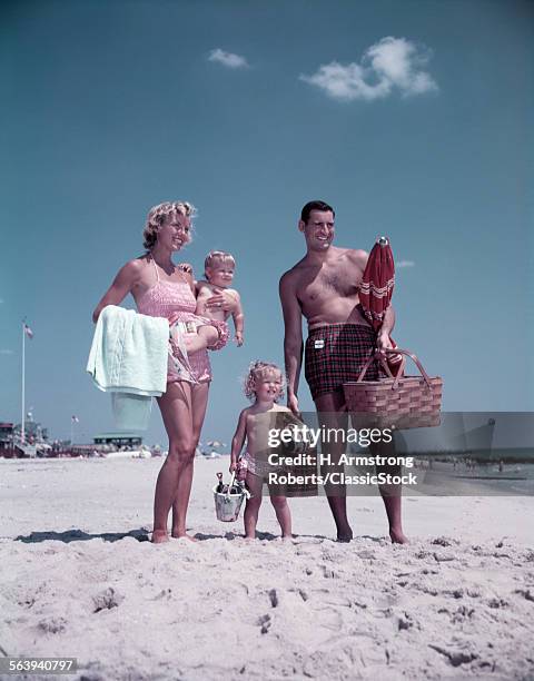 1950s FAMILY MAN WOMAN MOTHER FATHER CHILDREN BOY GIRL SON DAUGHTER STANDING SANDY BEACH WITH TOYS AND PICNIC BASKET