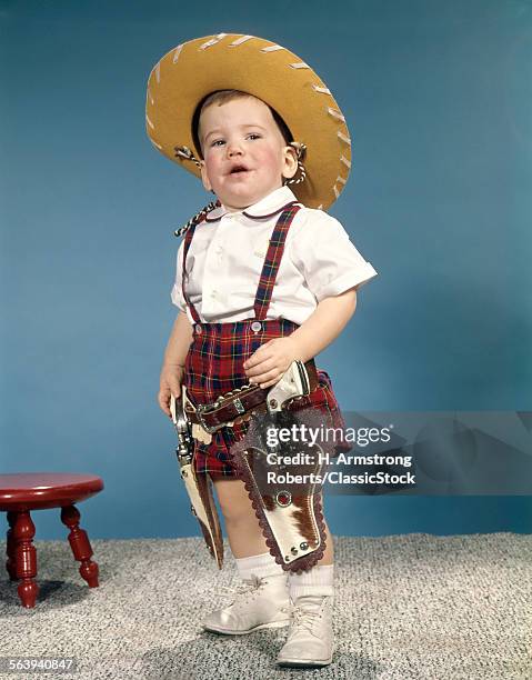 1950s 1960s LITTLE BOY WEARING COWBOY HAT AND TWO SIX GUN CAP PISTOLS HOLSTERS STANDING WITH ATTITUDE