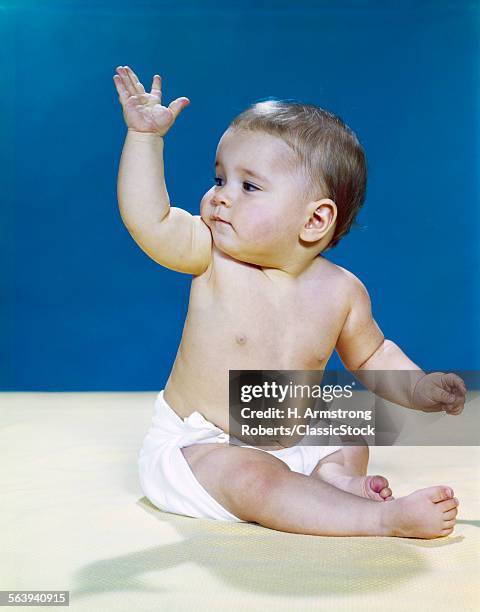 1960s BABY WEARING CLOTH DIAPER LOOKING OVER SHOULDER WAVING WITH RAISED ARM GESTURE