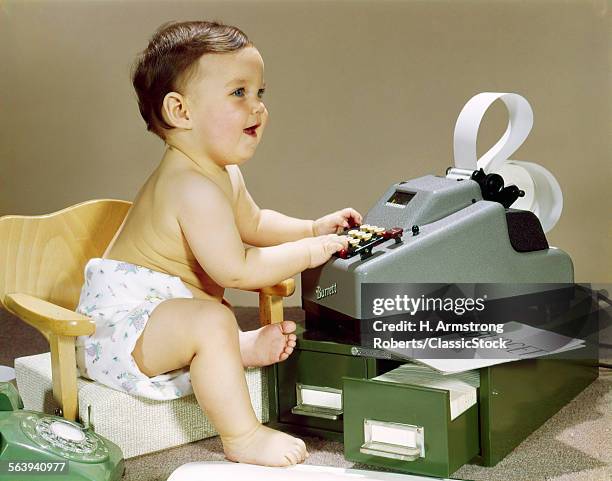 1960s SMILING ACCOUNTANT OFFICE WORKER BABY WEARING CLOTH DIAPER SITTING IN CHAIR USING ADDING MACHINE CALCULATOR