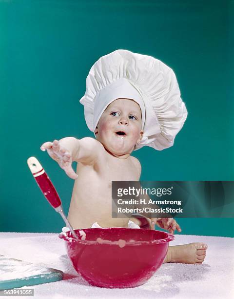 1960s BABY WEARING CHEF HAT WITH RED MIXING BOWL AND SPOON FUNNY FACIAL EXPRESSION
