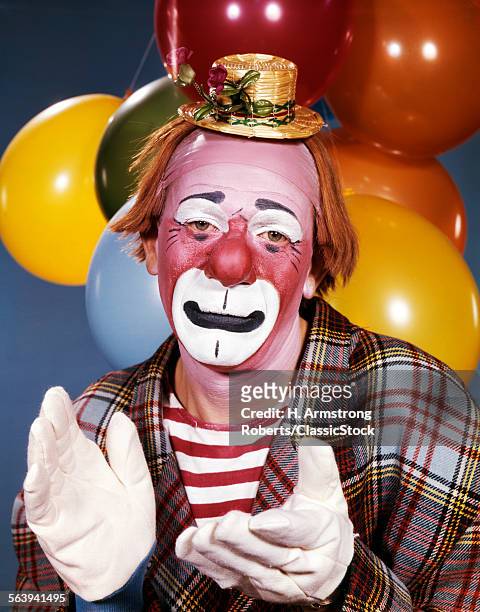 1960s PORTRAIT OF CLOWN WITH A SAD EXPRESSION WEARING TINY HAT CLAPPING HIS HANDS