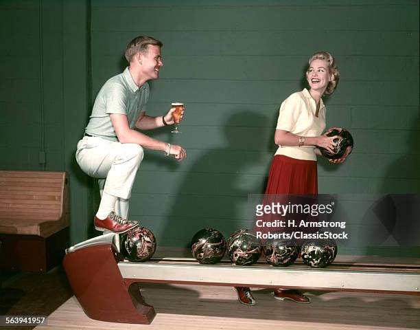1950s SMILING COUPLE IN BOWLING ALLEY WOMAN HOLDING BALL MAN WITH GLASS OF BEER I