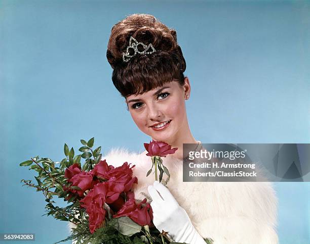 1960s TEENAGE BEAUTY QUEEN HOLDING RED ROSES WEARING FUR STOLE AND TIARA LOOKING AT CAMERA