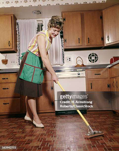1960s WOMAN IN APRON CLEANING KITCHEN FLOOR WITH SPONGE MOP