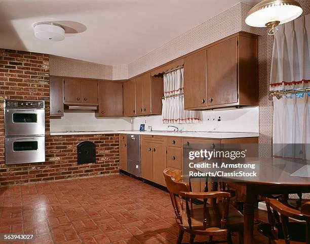 1980s KITCHEN WITH DARK WOODEN CABINETS BRICK WALL AND STAINLESS STEEL DOUBLE OVEN